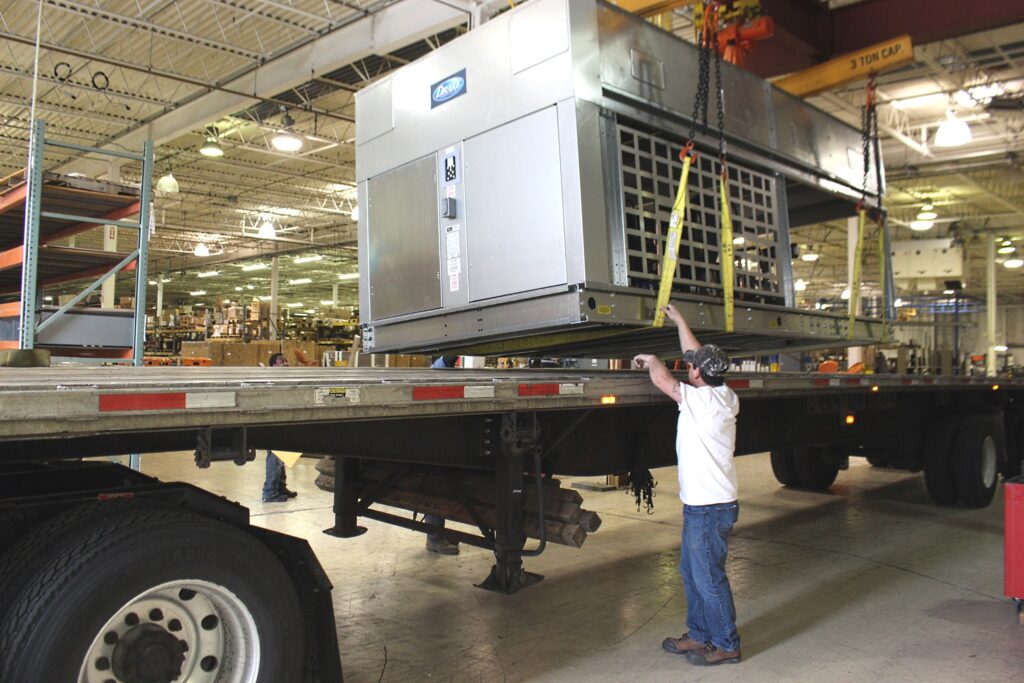 Drake employee loading large chiller unit onto flatbed truck trailer