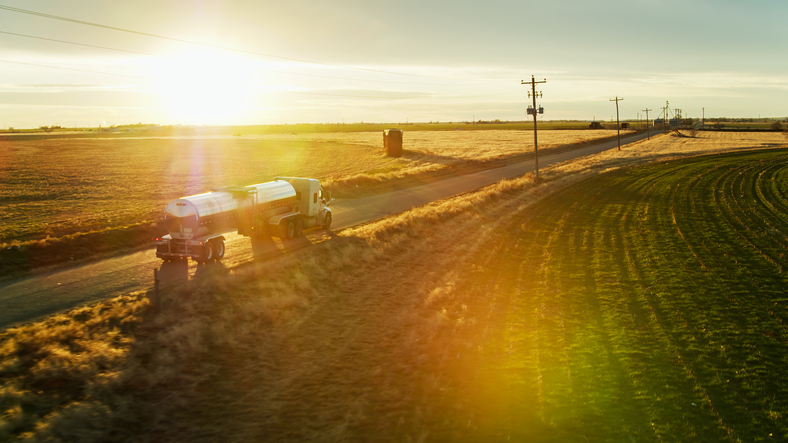 Aerial shot of a refrigerated milk tanker driving along a road between dairy farms, collecting milk in the evening.