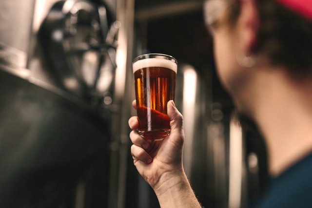 Brewery employee holding freshly poured pint of beer up to the light