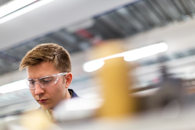 Engineering concept: male engineer wearing safety goggles at work, his head in focus with rest of image blurred